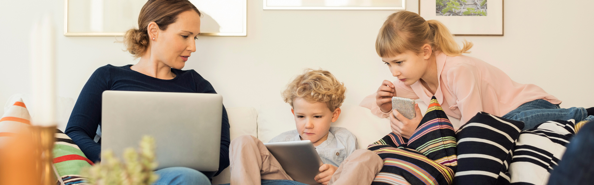 Mamma och två barn sitter i soffa och tittar på olika skärmar