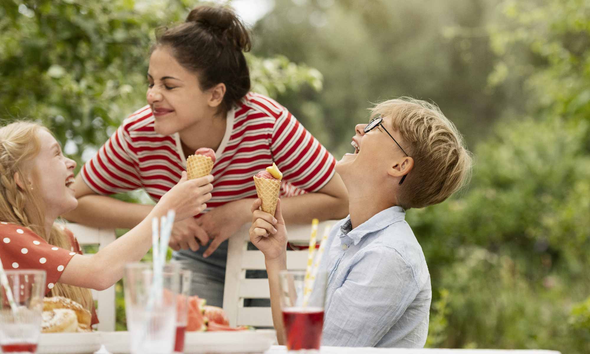 Mamma och två barn sitter ute i trädgården, skrattar och äter glass